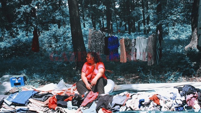 O femeie vinde îmbrăcăminte în mijlocul pădurii, unde se desfășoară o întreagă alee de produse ambulante, de la pantofi, la pitici de grădină și diverse antichități