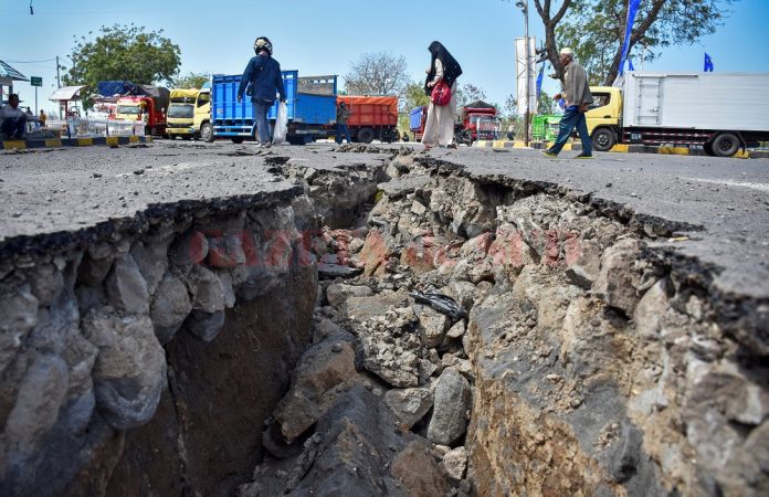 People walk near a road damaged by yesterday's large earthquake at Kayangan Port in Lombok