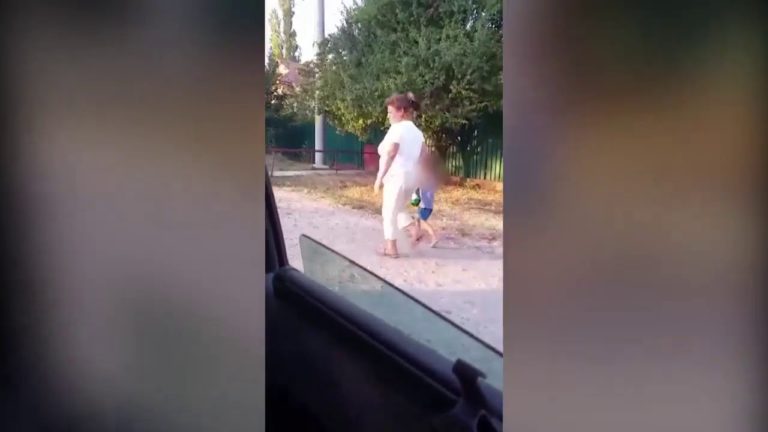 O mamă beată cade pe marginea drumului. Copilaşul îi ţine berea