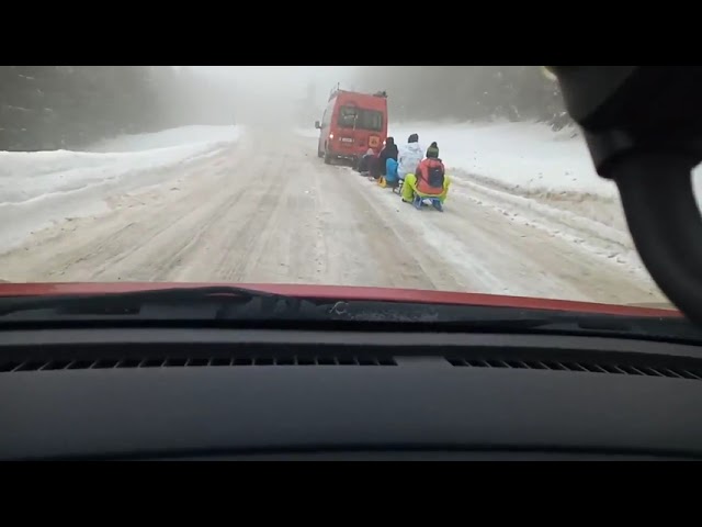 Șase sănii cu copii, trase de un microbuz pe un drum acoperit de zăpadă