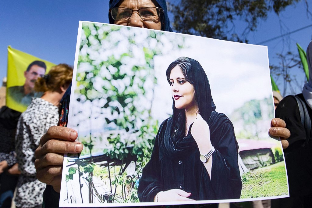 O femeie ține în sus o pancartă înfățișând o fotografie cu Mahsa Amini, de 22 de ani