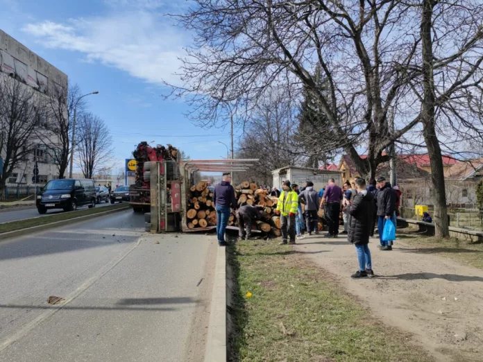 Remorcă plină cu lemne, răsturnată pe trotuar. Trei persoane, rănite