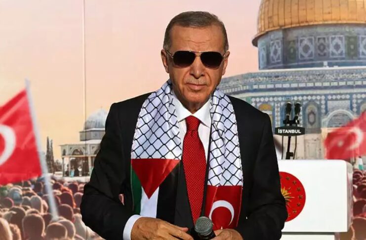 Președintele turc Tayyip Erdogan, purtând o eșarfă cu steagul palestinian și turcesc, stă pe scenă în timpul unui miting organizat de partidul AKP în solidaritate cu palestinienii din Gaza, la Istanbul