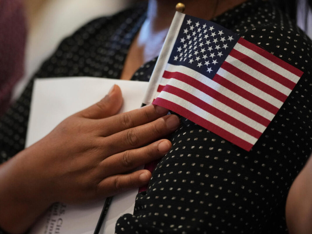 O femeie ține în mână un steag american în timp ce ea și candidați din alte țări se pregătesc să depună jurământul de cetățenie în comemorarea Zilei Independenței în timpul unei ceremonii de naturalizare din San Antonio, 3 iulie 2025