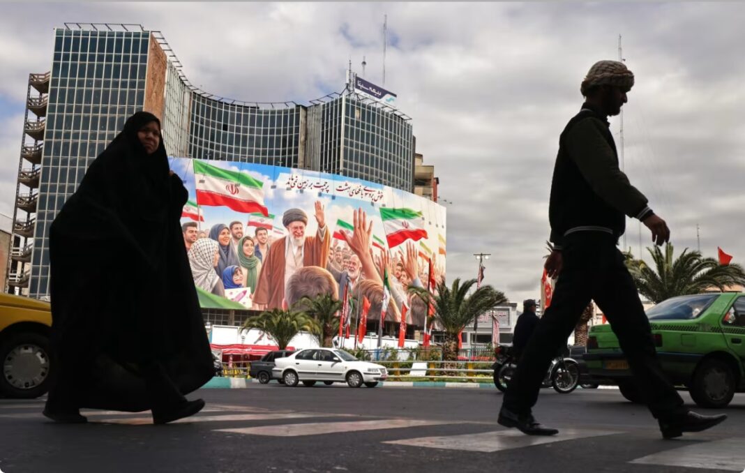 Navetiștii își croiesc drum pe lângă un panou publicitar gigantic cu liderul suprem iranian ucis, Ali Khamenei, în Piața Valiasr din Teheran, pe 19 aprilie 2026 (Atta Kenare/AFP/Getty Images)